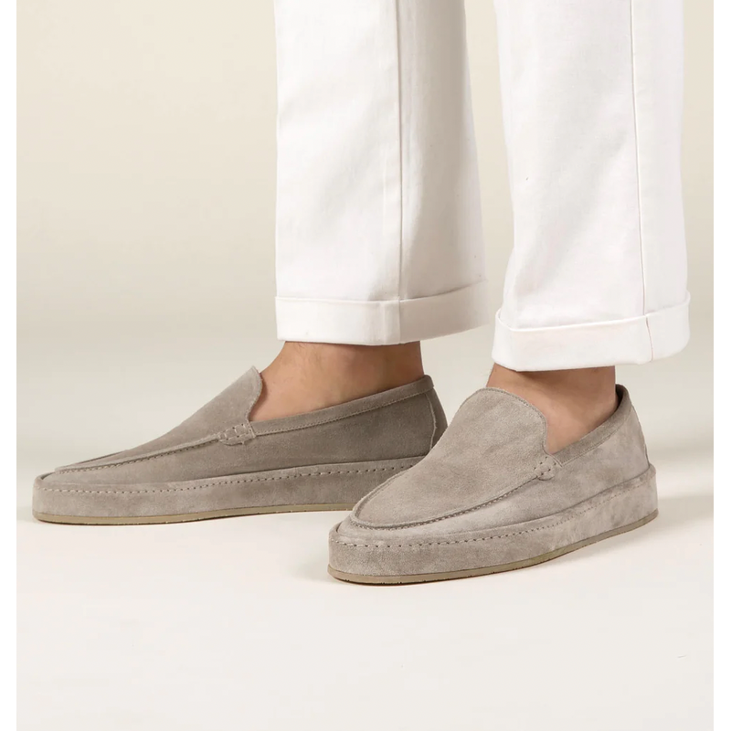 Beige men's slip-on loafers worn with white trousers