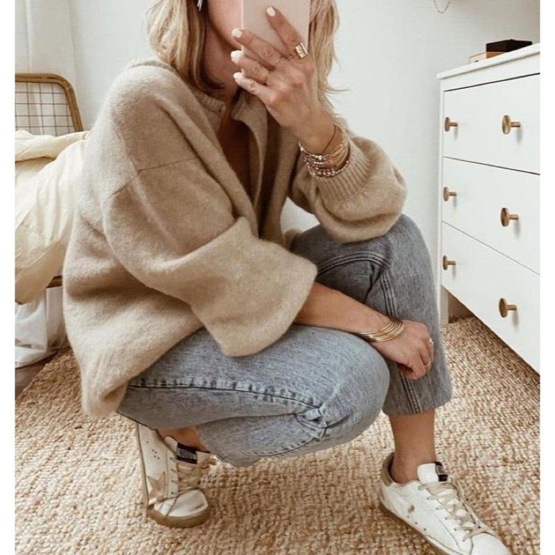 Woman crouching in a beige oversized cardigan and jeans