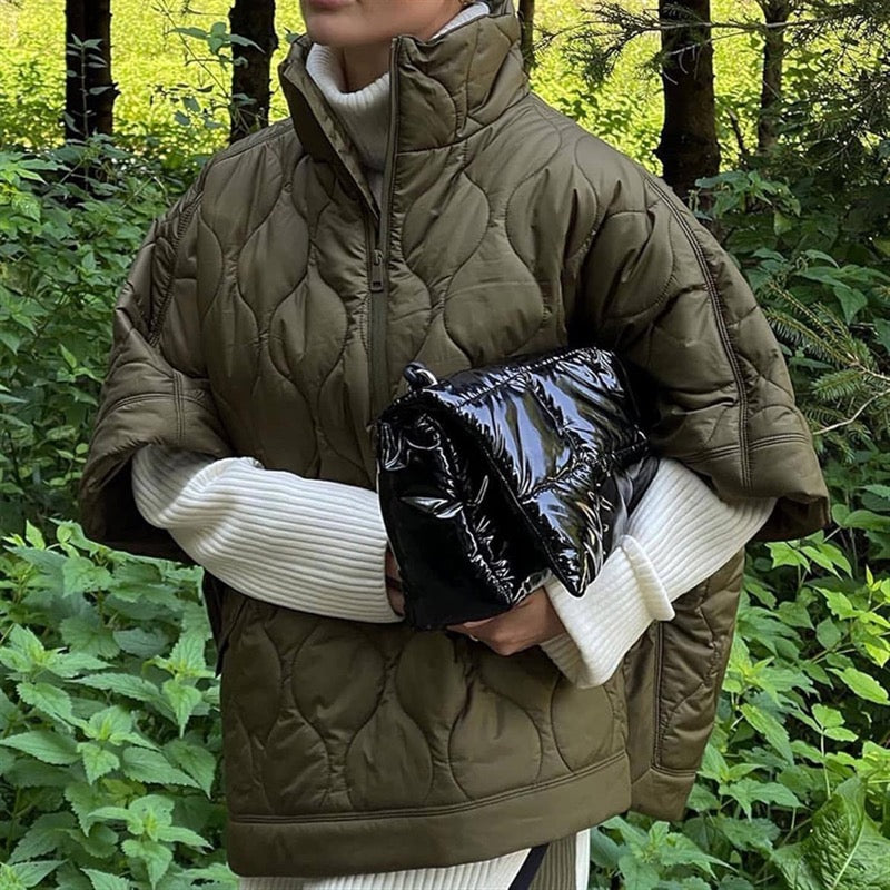 Olive green quilted cape jacket with high zipped stand collar over a white knit